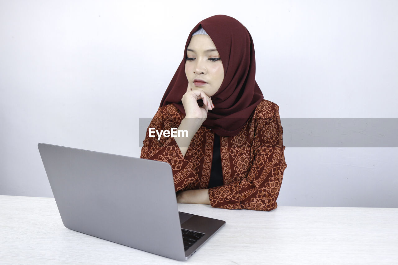 WOMAN LOOKING AT CAMERA WHILE SITTING IN LAPTOP