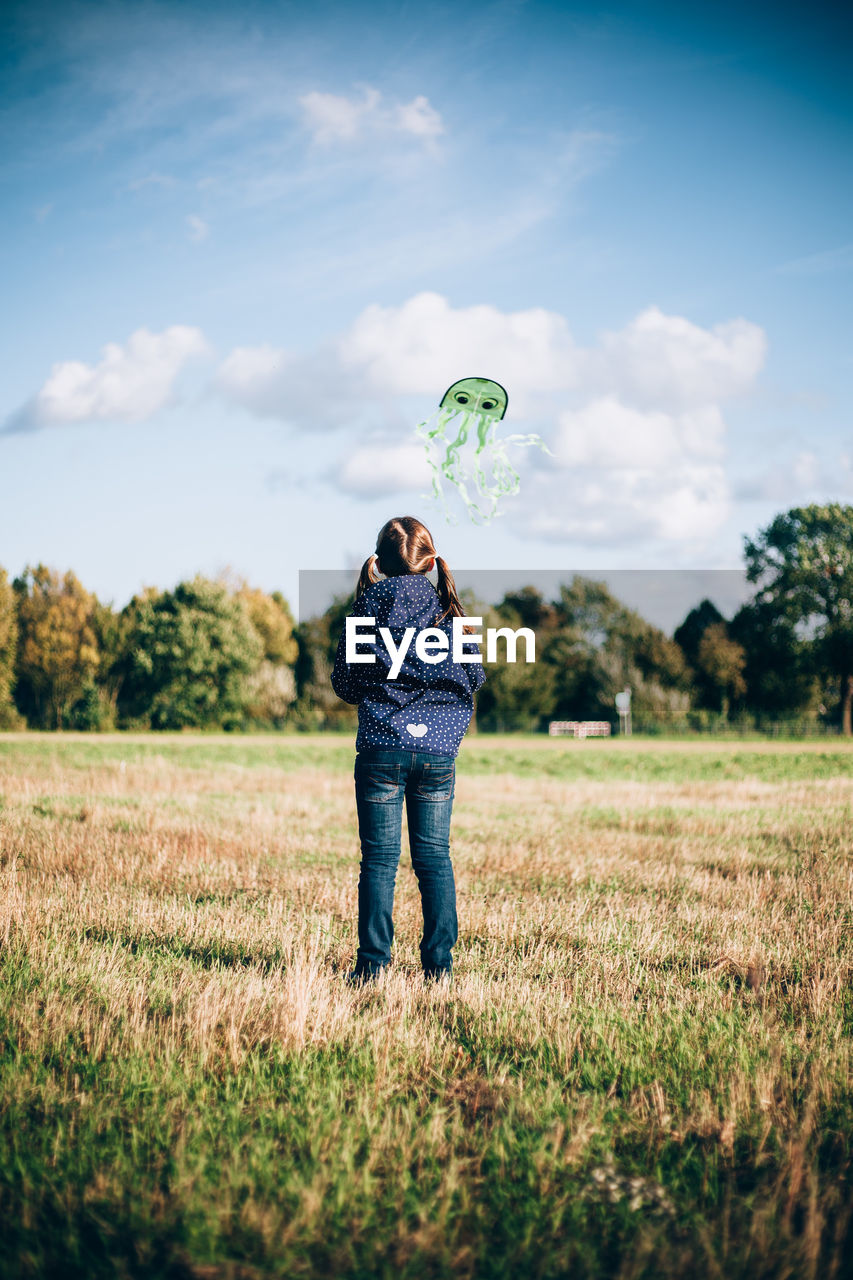 Rear view of girl flying kite on land against sky