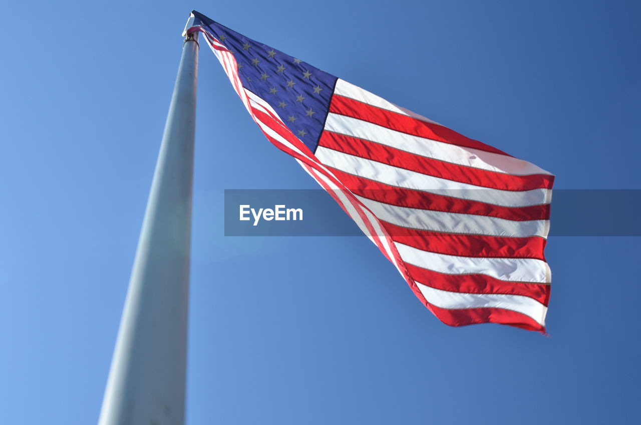 Low angle view of american flag waving against clear blue sky