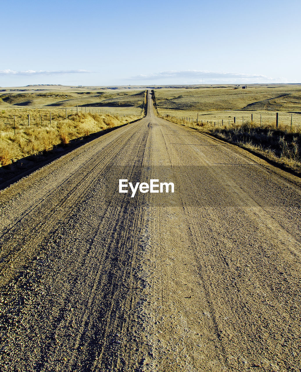Empty road amidst field against clear sky