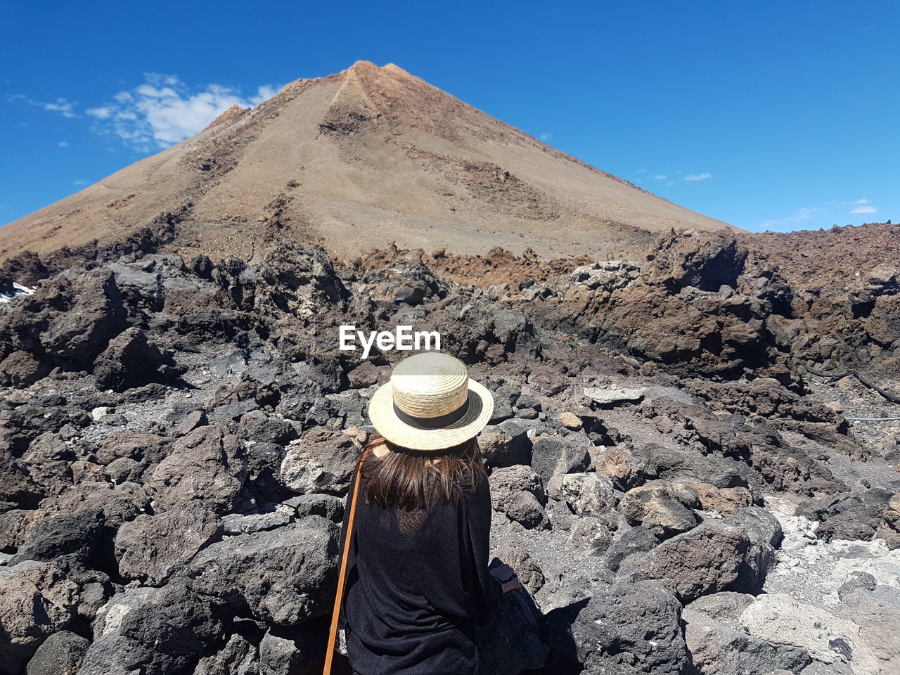 Rear view of woman wearing hat standing by rocks against blue sky