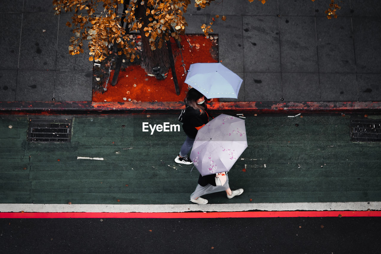 FULL LENGTH REAR VIEW OF WOMAN WALKING ON FOOTPATH IN CITY