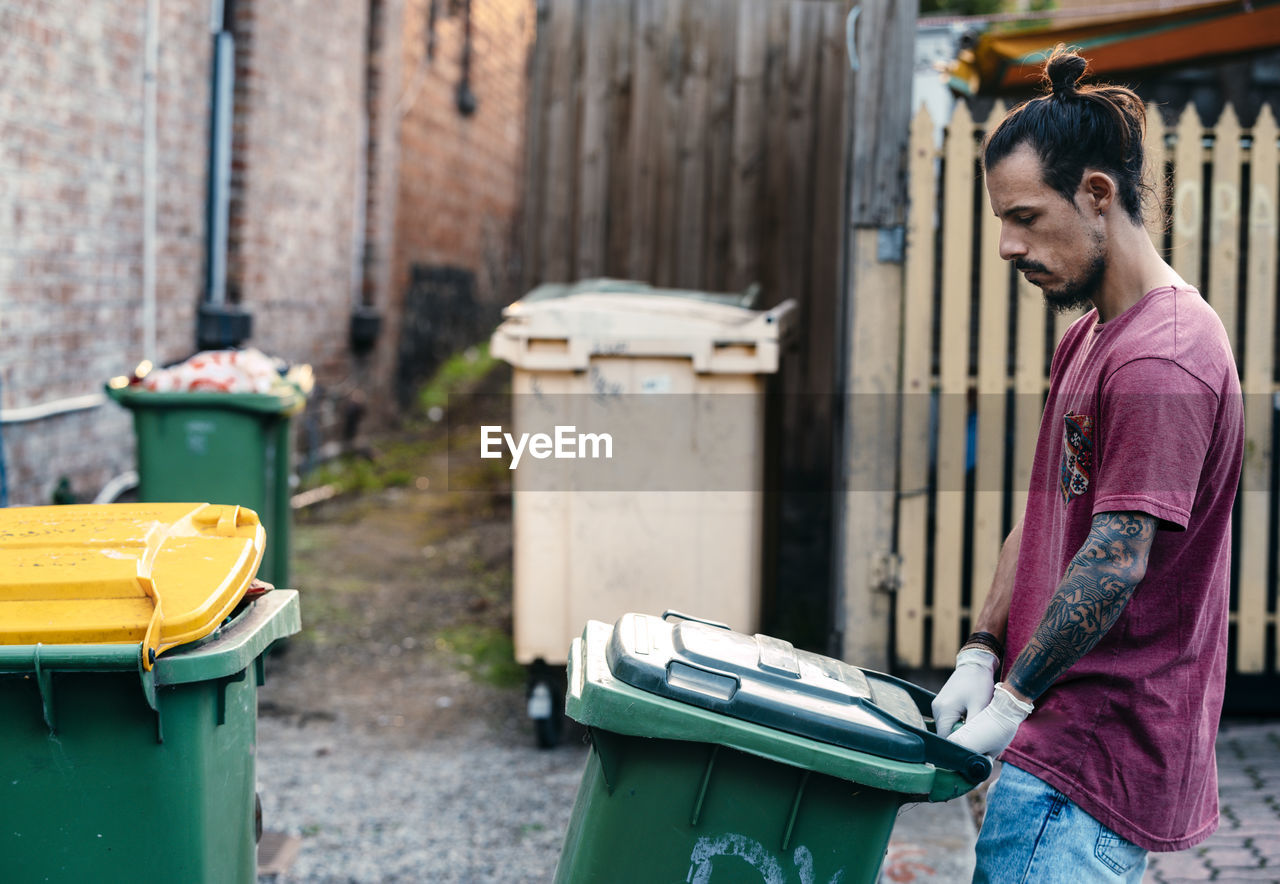 Side view of man holding garbage bin standing on street