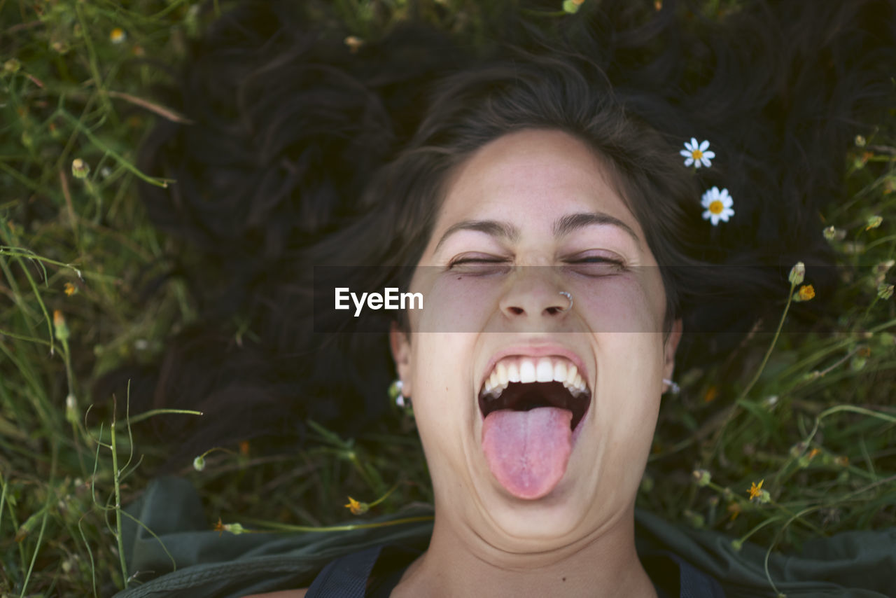 Portrait of a young woman lying in the grass with flowers in her hair. she sticks out her tongue with a happy expression