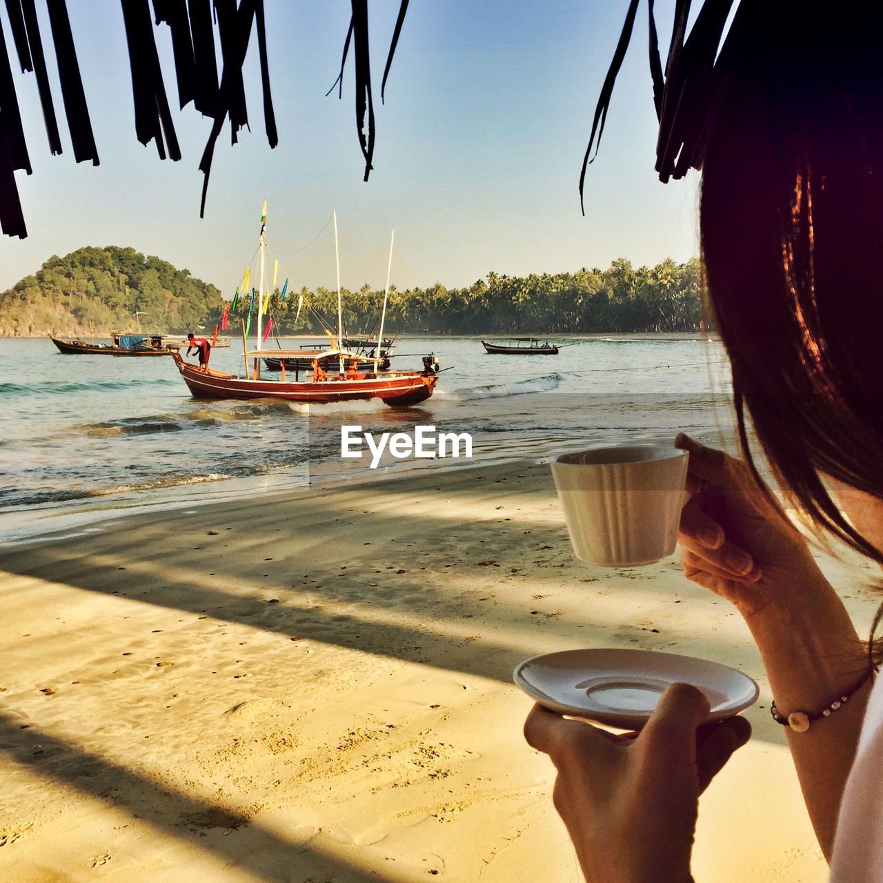 Cropped image of woman holding coffee cup on beach