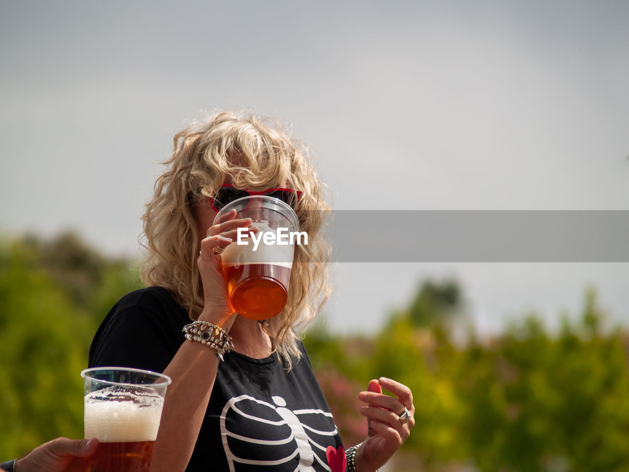 Cropped hand of man and woman drinking beer in glass against sky