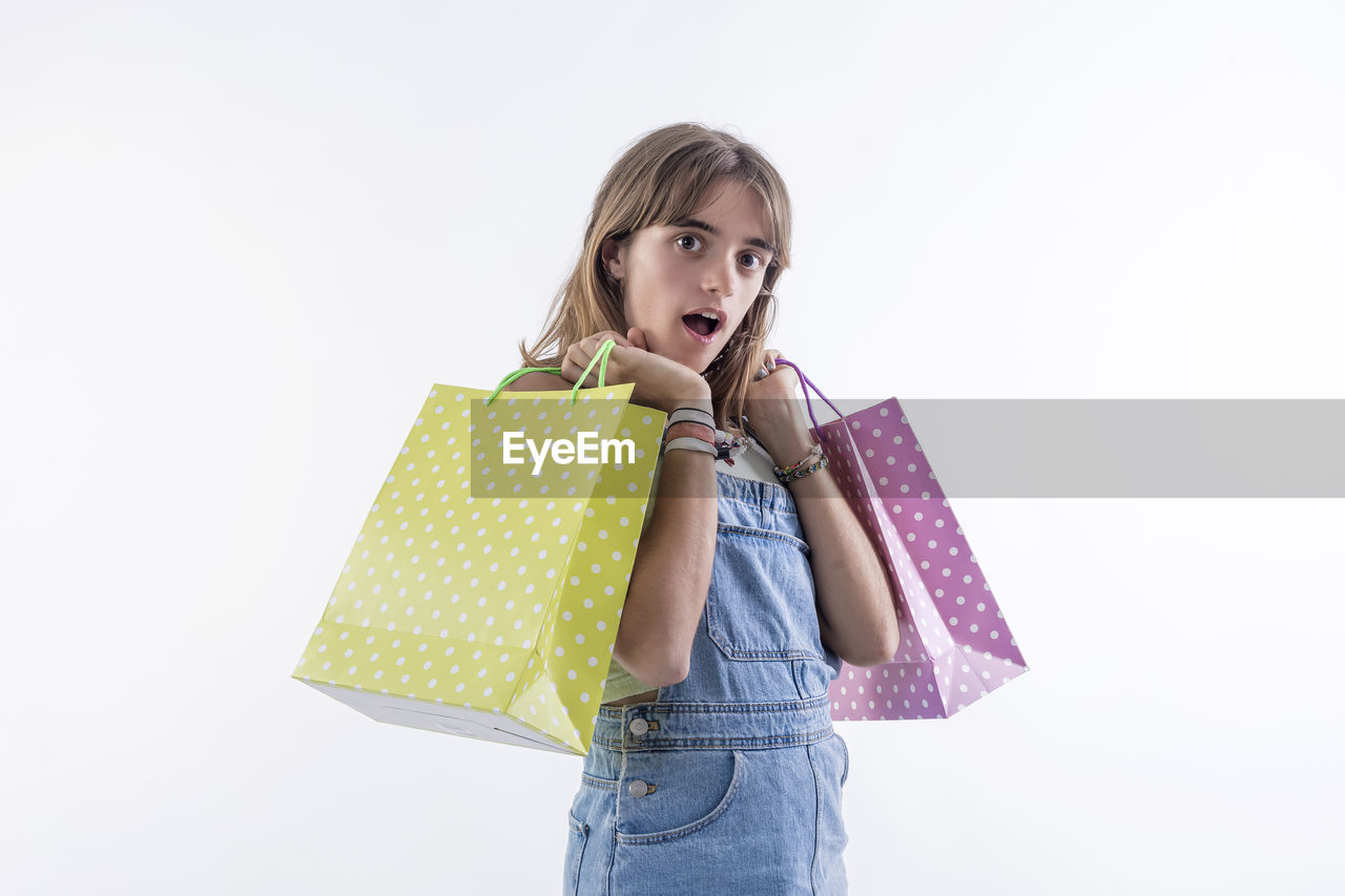 one person, shopping bag, bag, holding, women, handbag, tote bag, white background, studio shot, pattern, shopping, casual clothing, consumerism, indoors, carrying, child, clothing, emotion, front view, portrait, copy space, childhood, female, happiness, retail, blond hair, standing, fashion accessory, surprise, gift, adult, spending money, pink, shoulder bag, person, young adult, outerwear, looking, lifestyles, smiling, cut out, looking at camera, hairstyle, customer