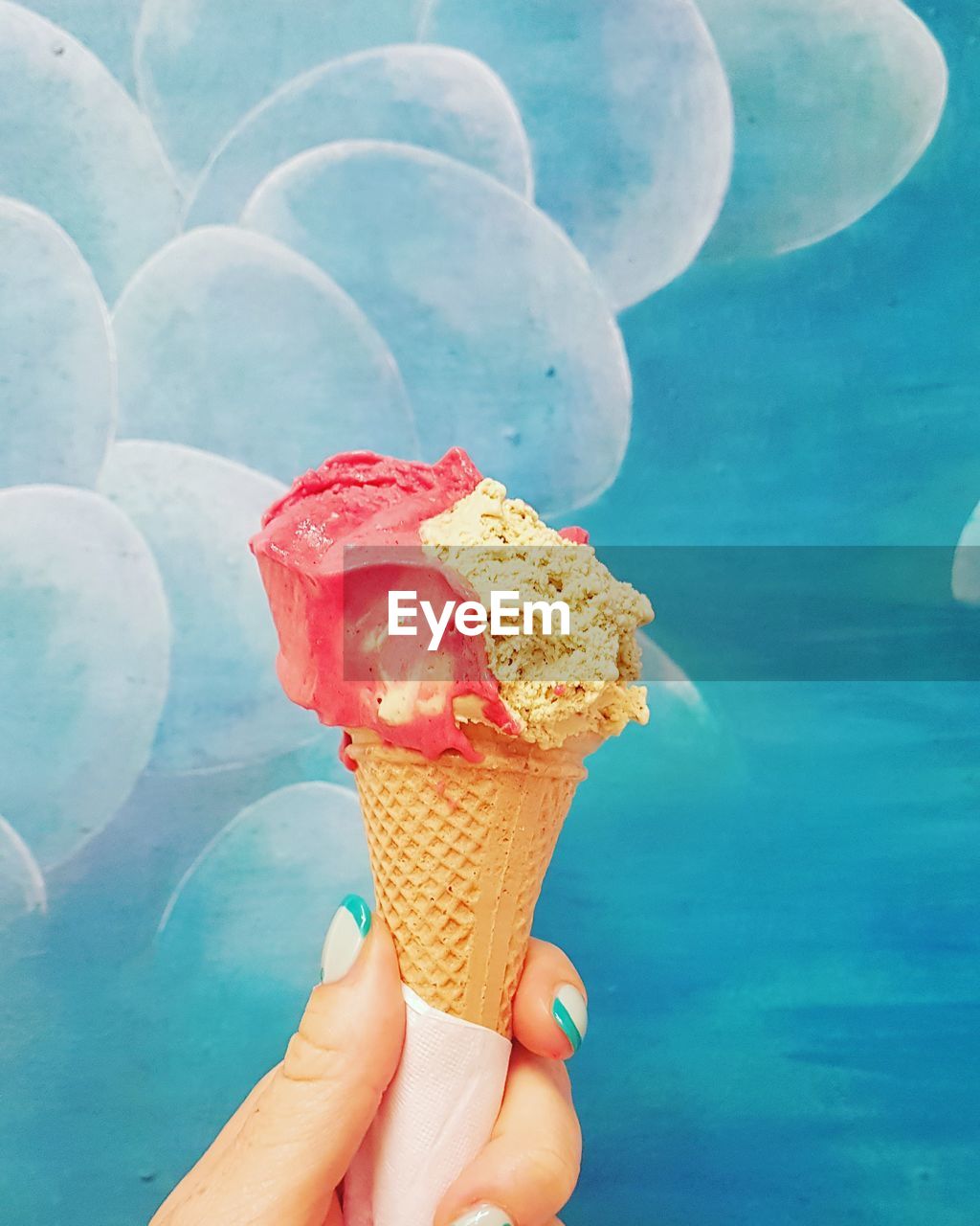 CROPPED HAND HOLDING ICE CREAM CONE AGAINST BLUE SKY