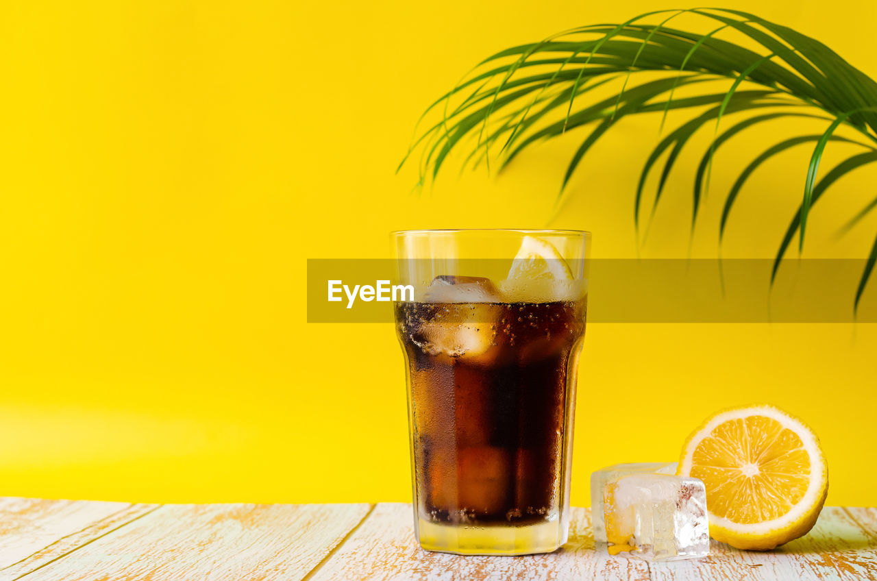 A glass of cold soft drink with lemon on wooden floor with coconut leaf. summer drink concept.