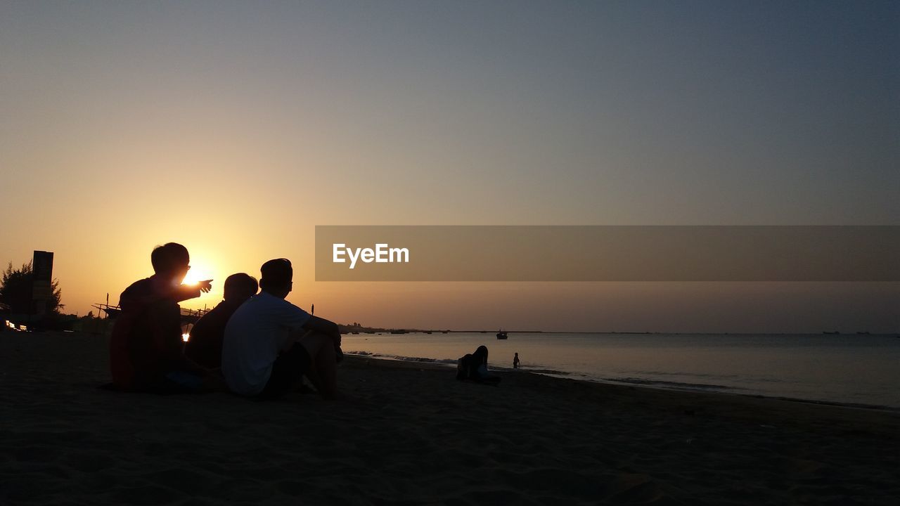 PEOPLE SITTING ON BEACH DURING SUNSET