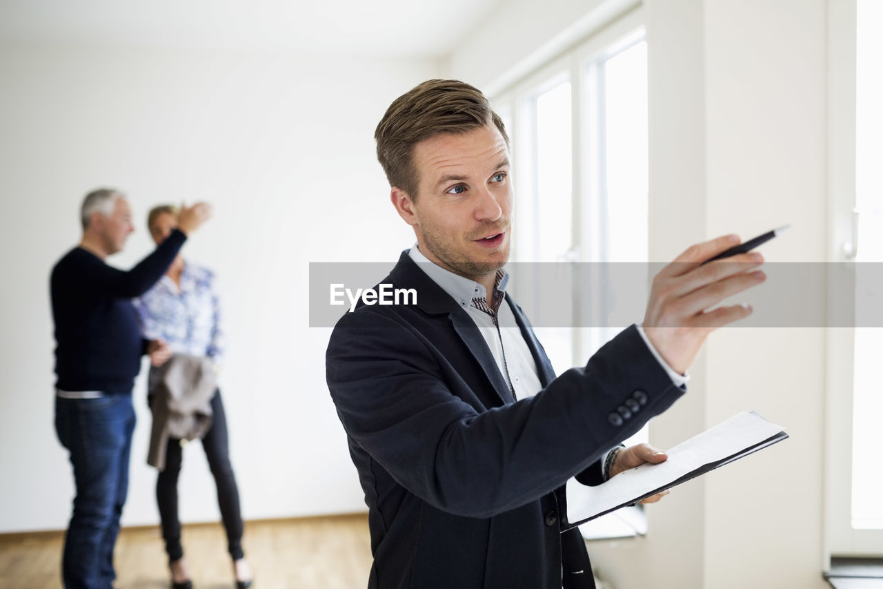 Real estate agent examining house with couple discussing in background