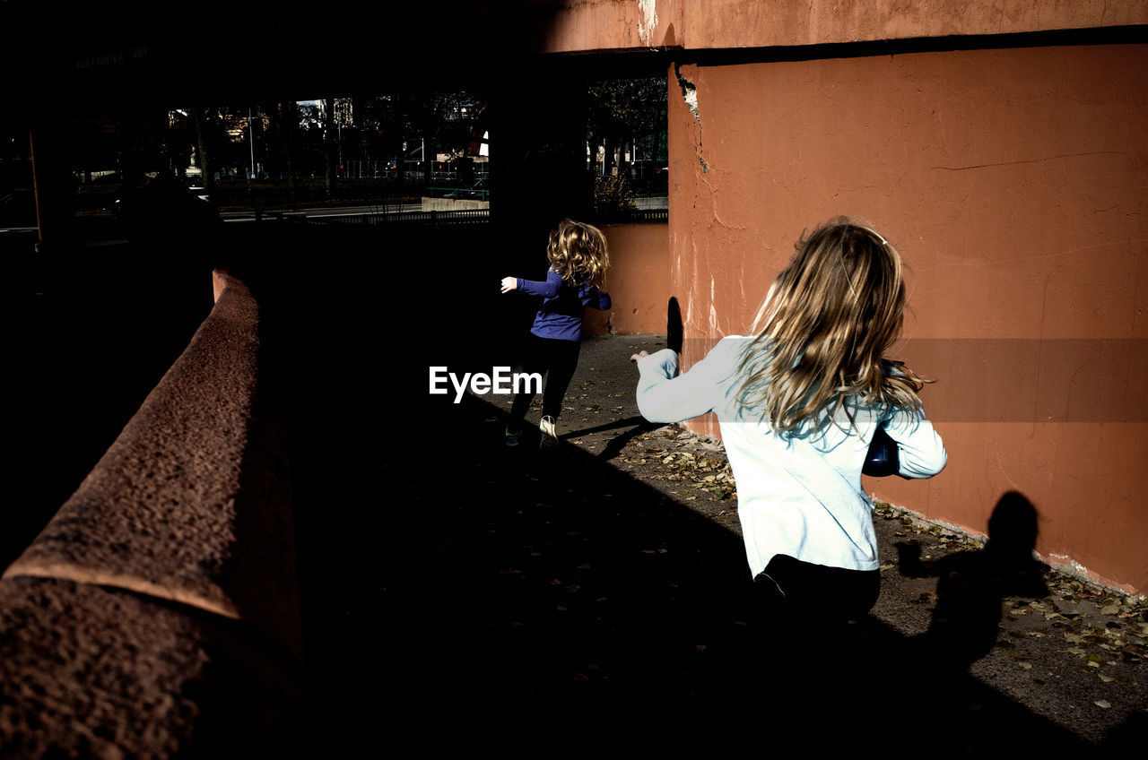 Rear view of girls running against wall