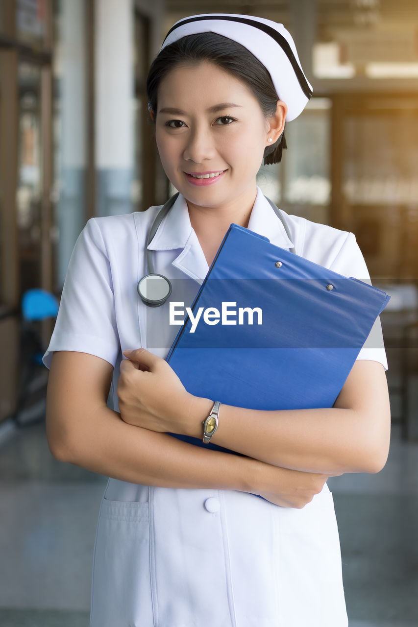 Portrait of female doctor holding file while standing in hospital