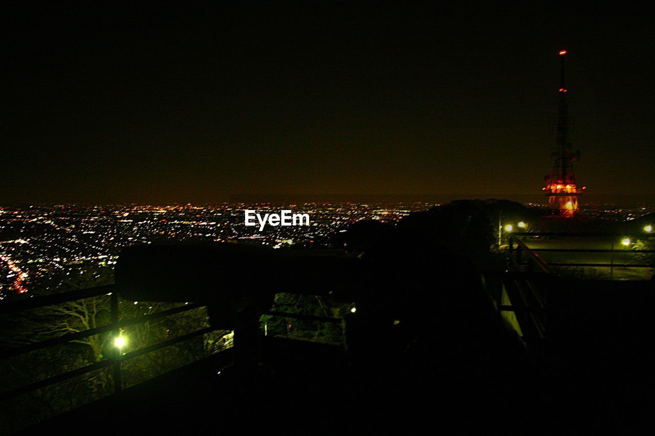 Binoculars at observation point against illuminated cityscape at night