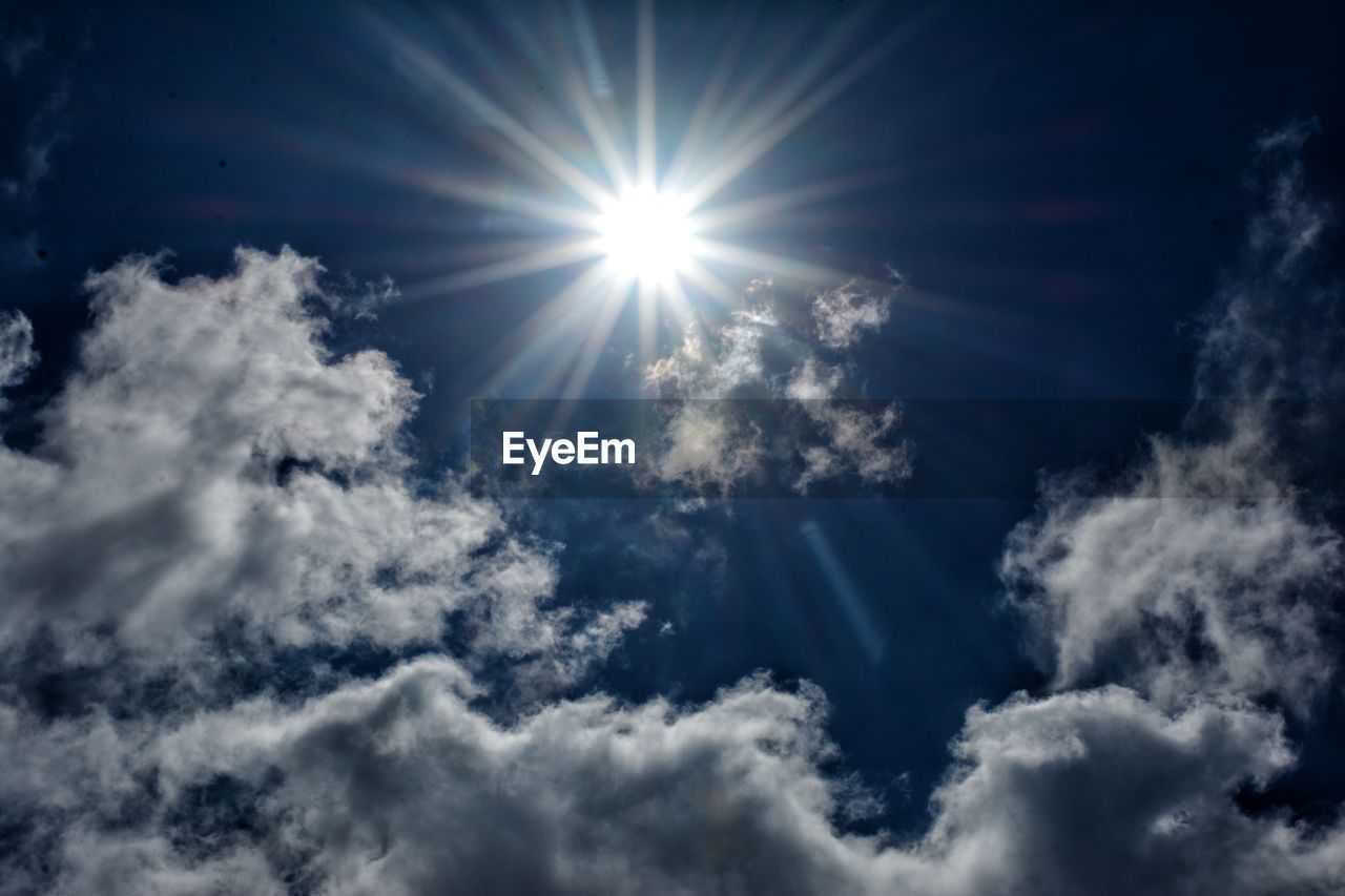 LOW ANGLE VIEW OF SUNLIGHT STREAMING THROUGH CLOUDS IN SKY