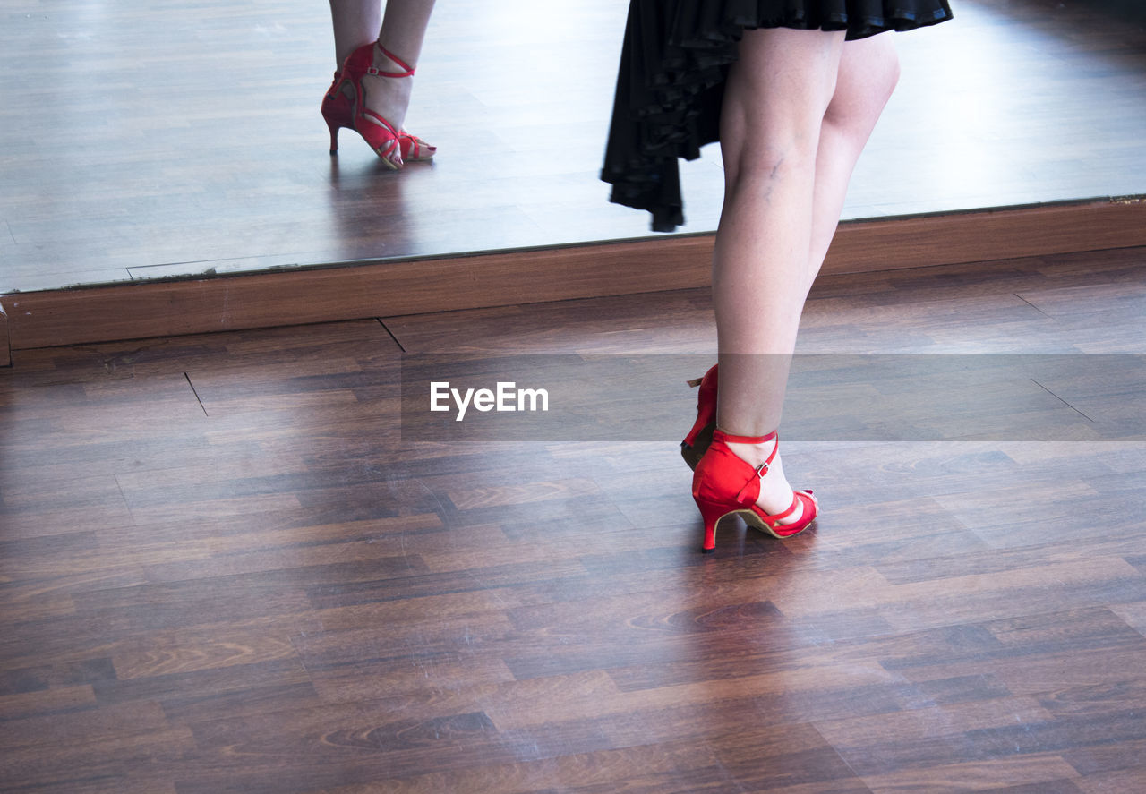 Low section of woman in high heels standing on hardwood floor