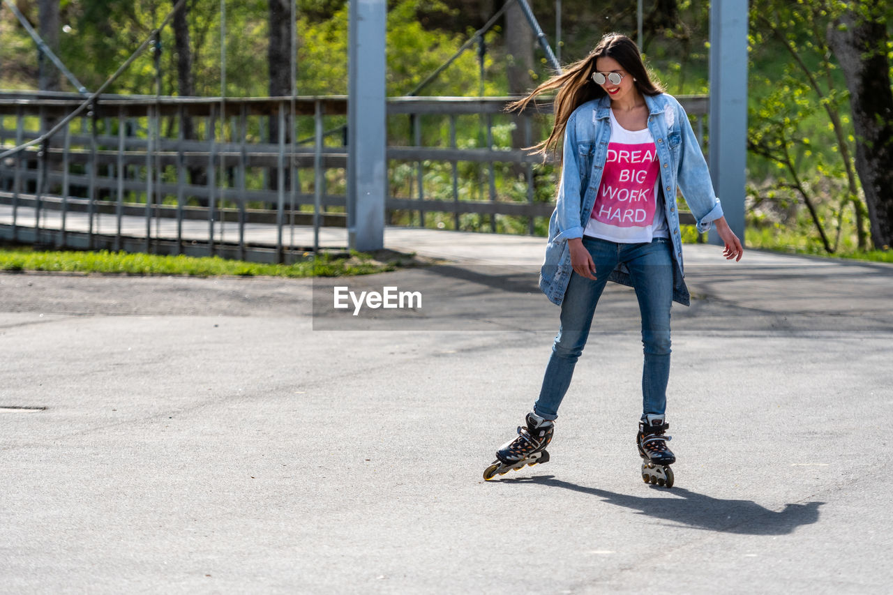 FULL LENGTH OF WOMAN WITH SKATEBOARD STANDING ON ROAD