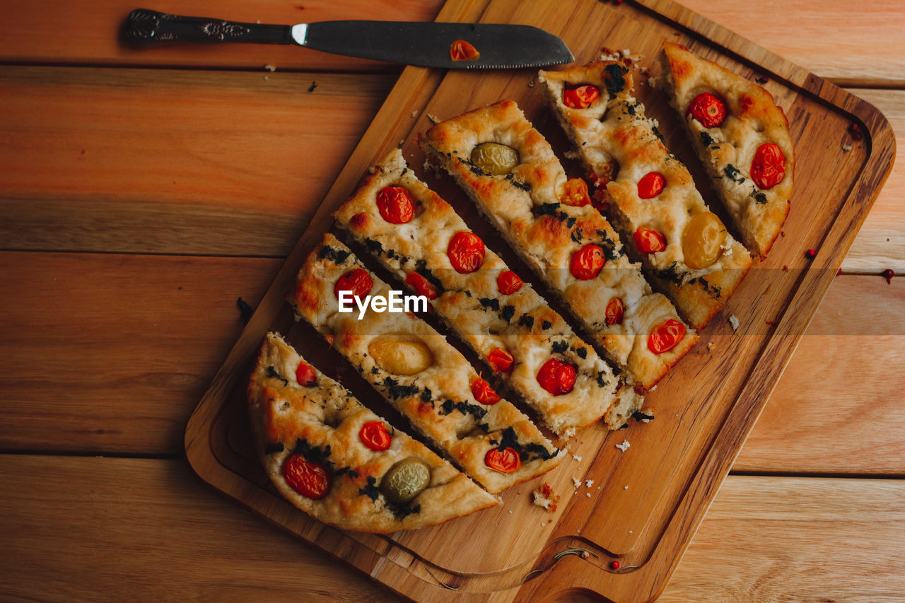 Homemade italian focaccia cut into slices, with tomato and olive oil on a rustic wooden background.
