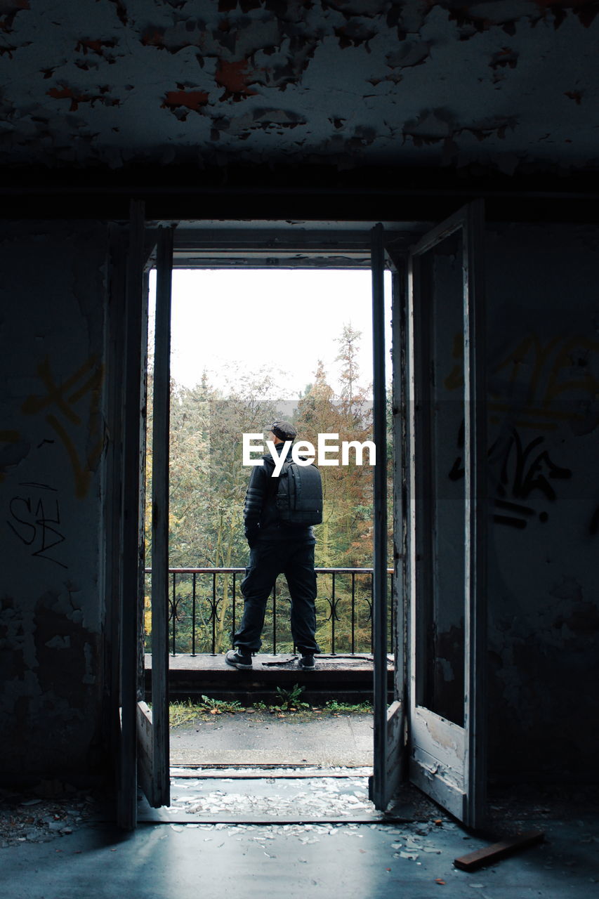 FULL LENGTH OF MAN STANDING BY WINDOW OF ABANDONED BUILDING