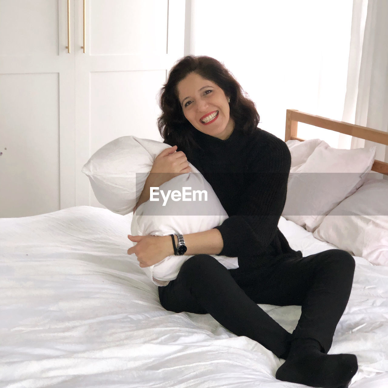 Portrait of smiling young woman sitting on bed at home