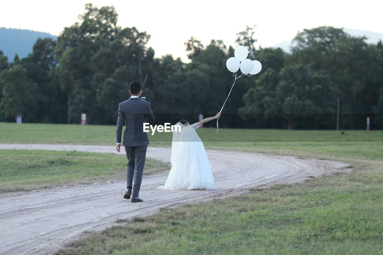 REAR VIEW OF COUPLE HOLDING HANDS ON FOOTPATH