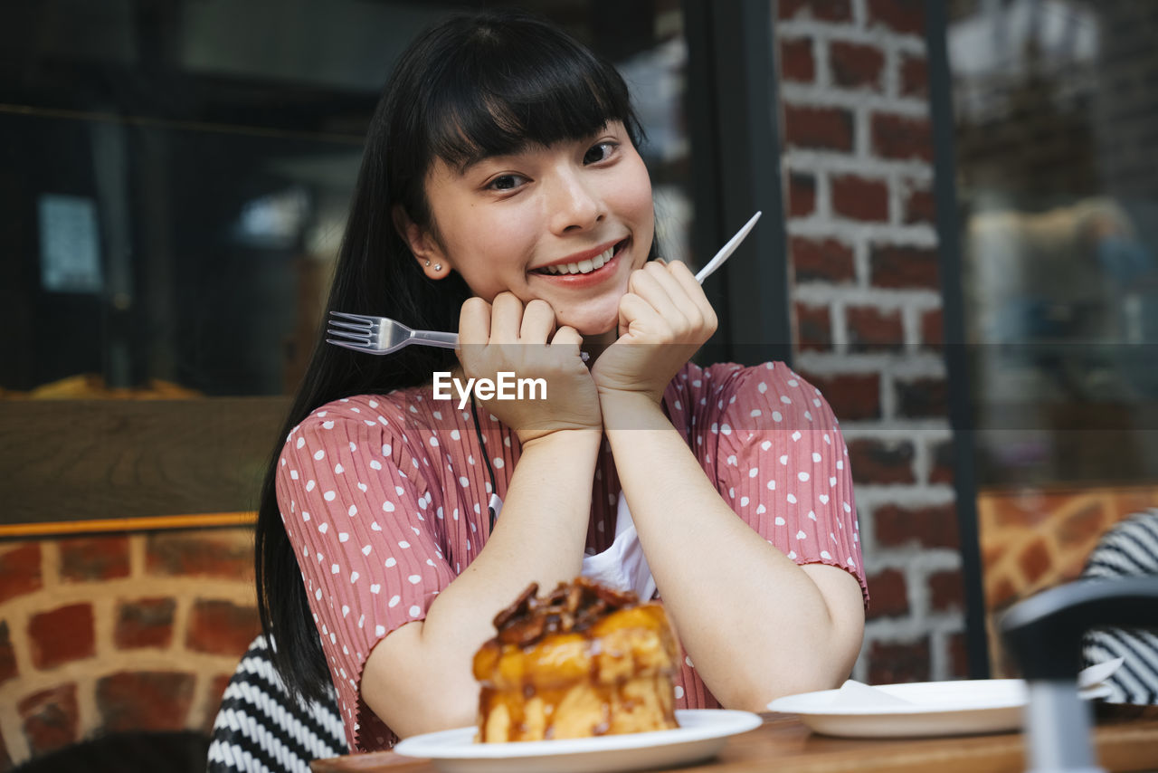PORTRAIT OF A SMILING YOUNG WOMAN SITTING AT RESTAURANT