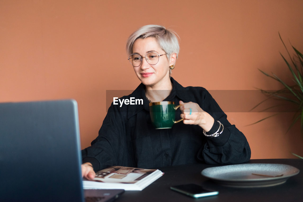 Fashion woman in black shirt working in modern work place or office with laptop and coffe cup