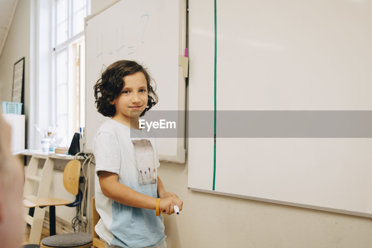 Smiling boy standing by whiteboard at classroom