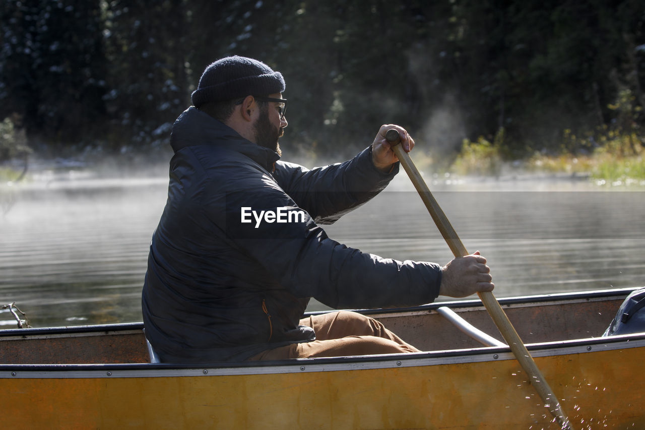 Close up of bearded man paddling canoe on a foggy lake in canada