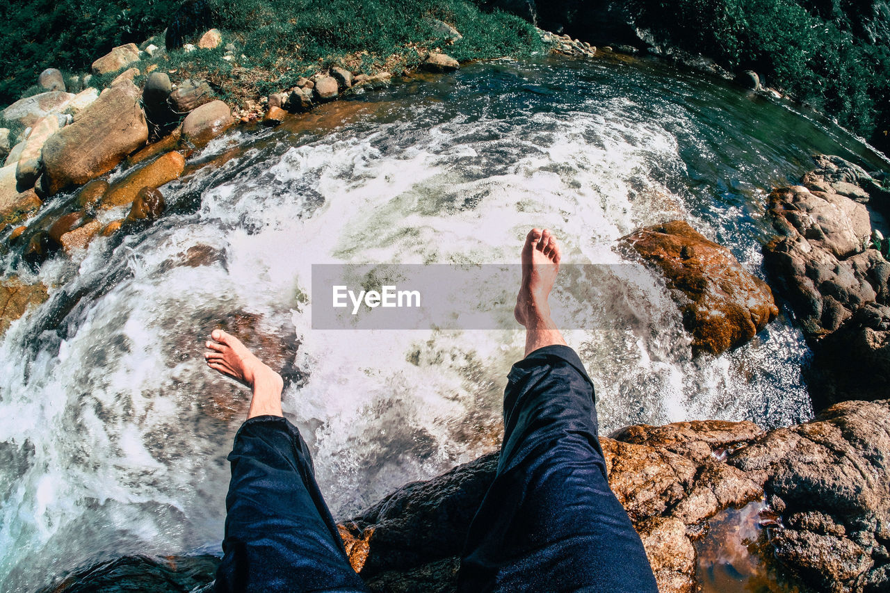 Low section of person sitting on cliff by stream