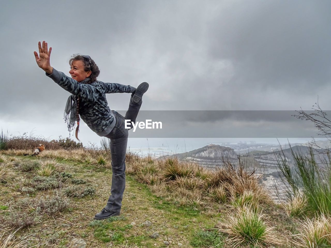 Full length portrait of woman exercising while standing on grass against sky