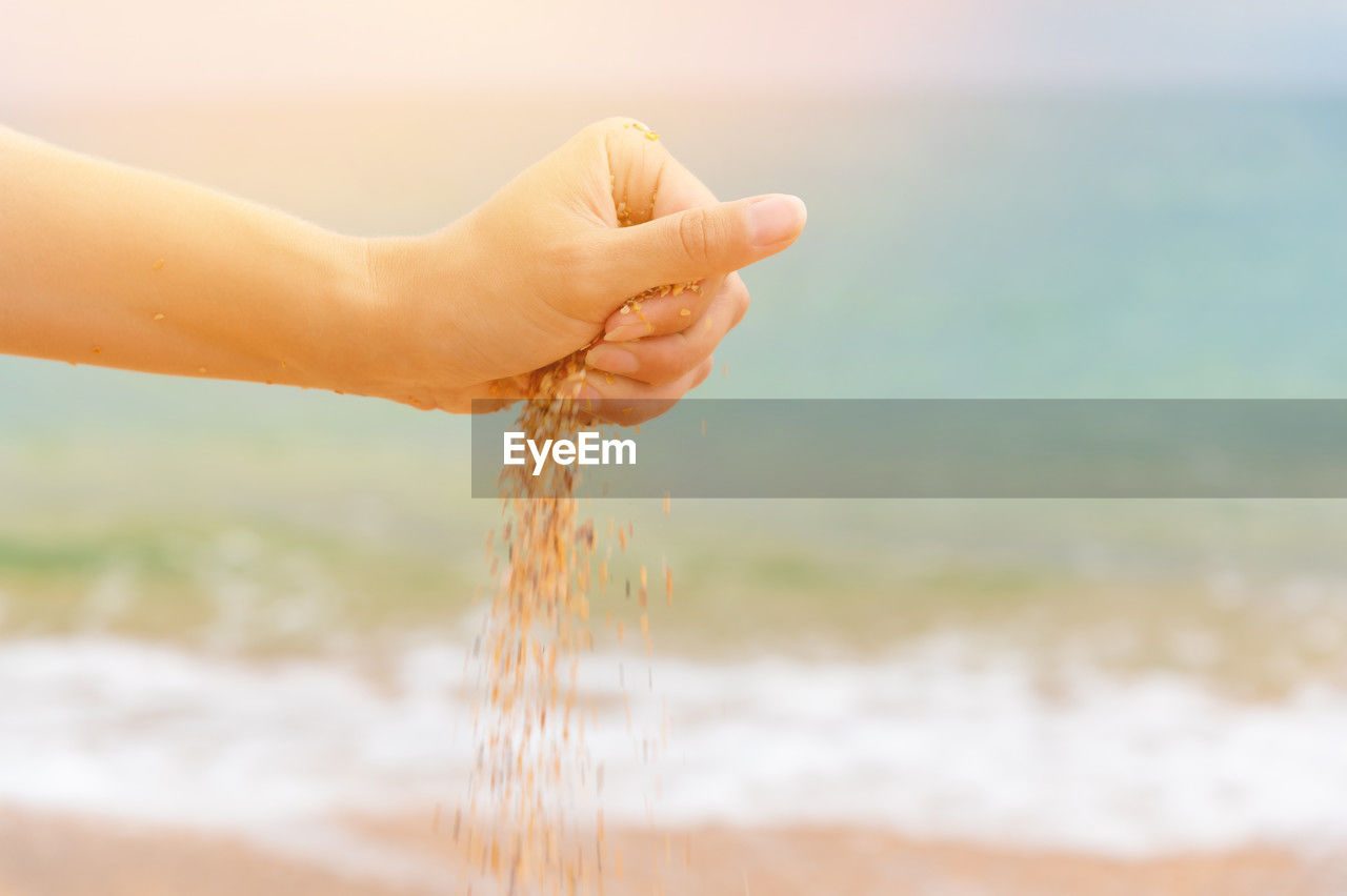 Sand falls from woman hands on sea summer background