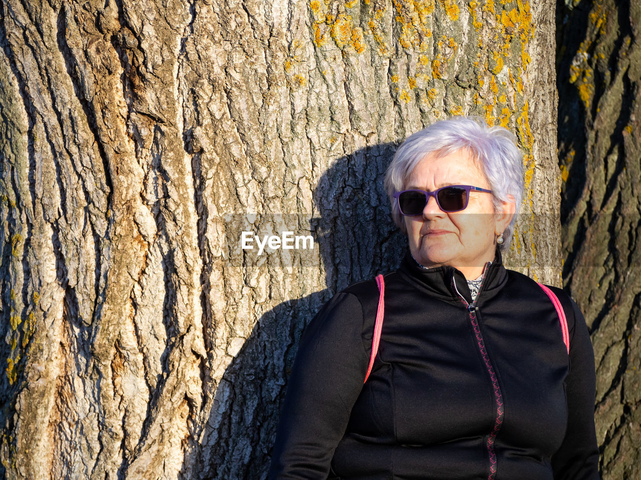 Senior woman standing against tree trunk