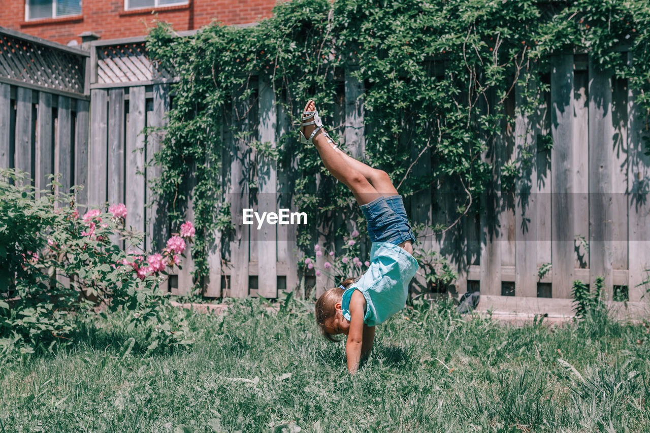 Full length of girl doing handstand against plants in yard