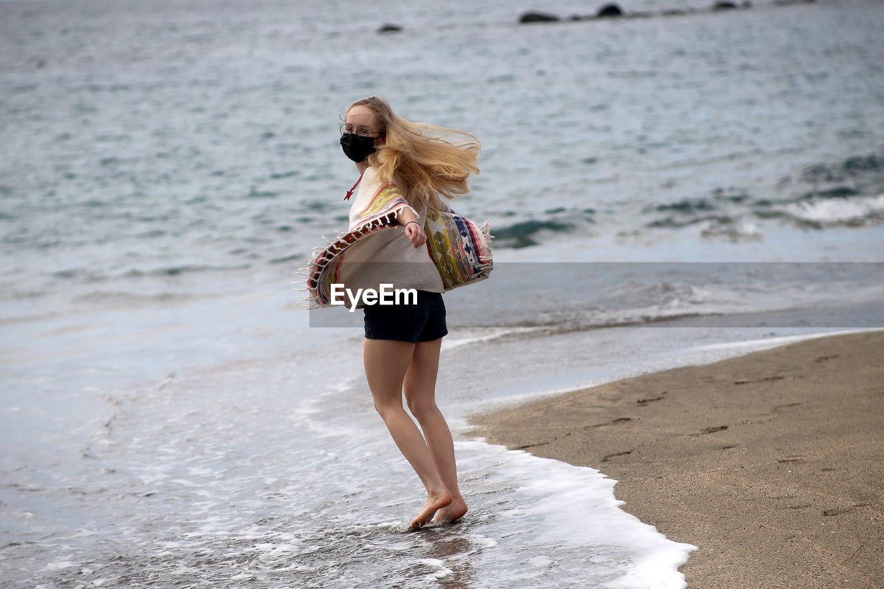 Side view of woman wearing mask walking at beach