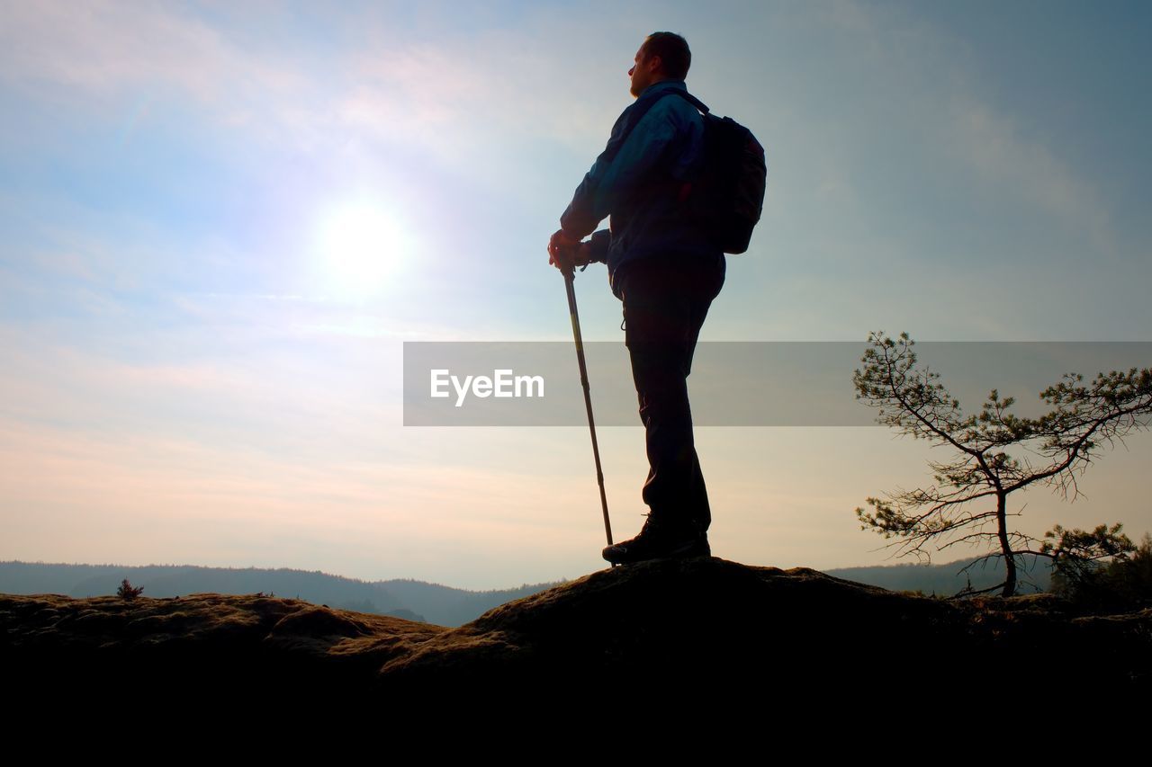 Tourist in windcheater with sporty trecking poles in hands stand on rocky view point