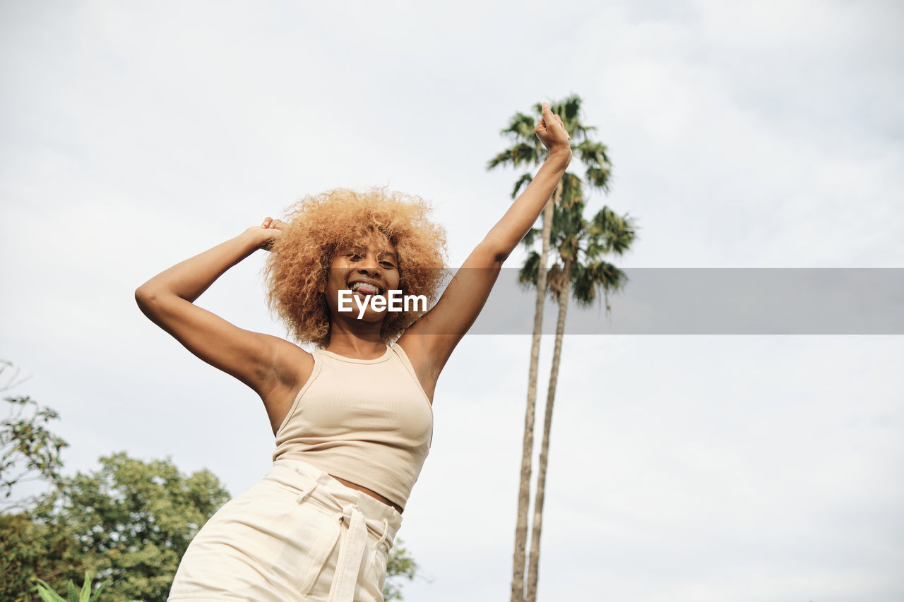 Carefree woman with arms raised standing in front of sky