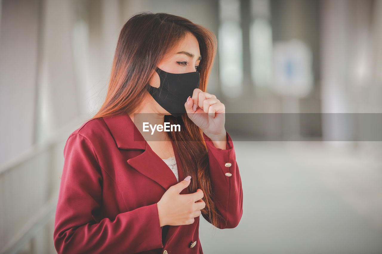 Woman wearing mask coughing while standing indoors