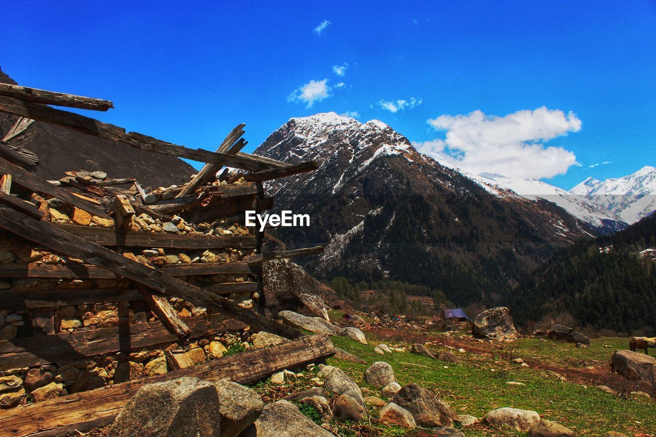 Scenic view of ruined hut with snowcapped mountains against blue sky