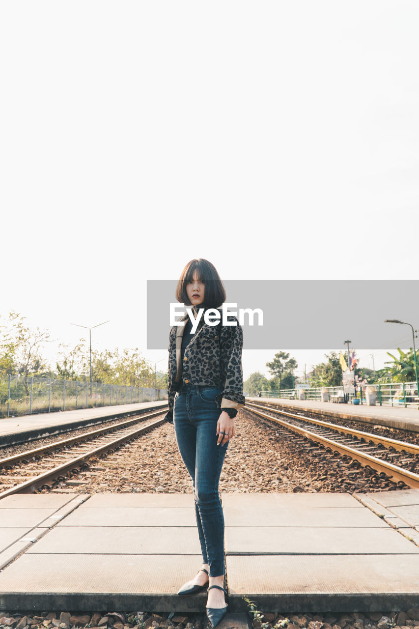 Full length portrait of woman standing on railroad tracks against sky