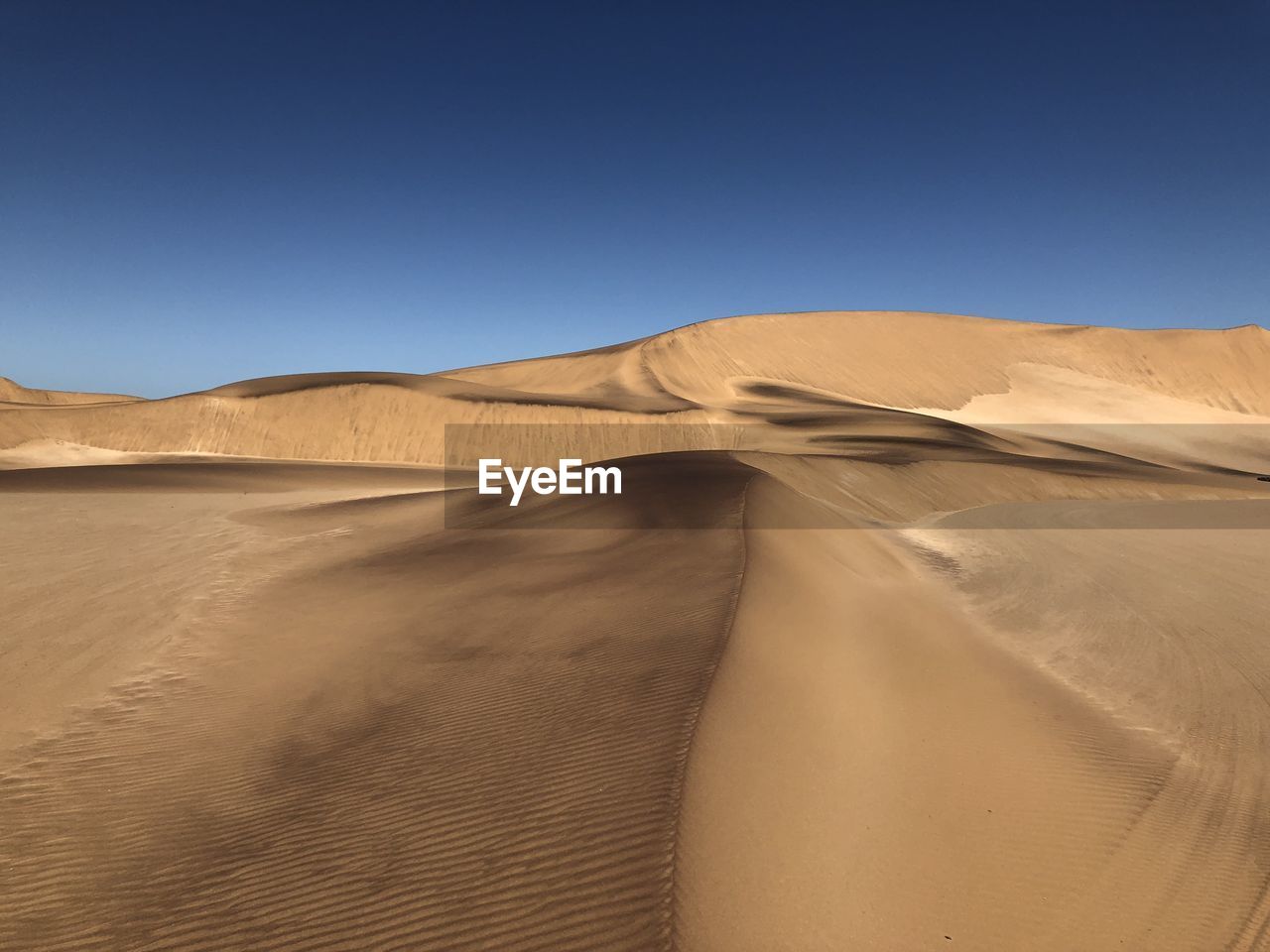 Sand dunes in desert against clear blue sky