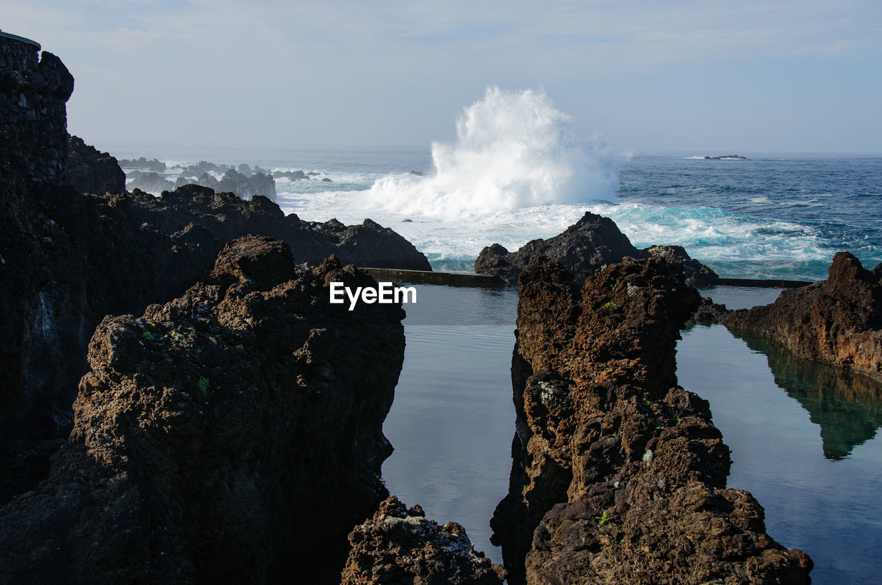 Wave splashing in sea with rock formation against sky