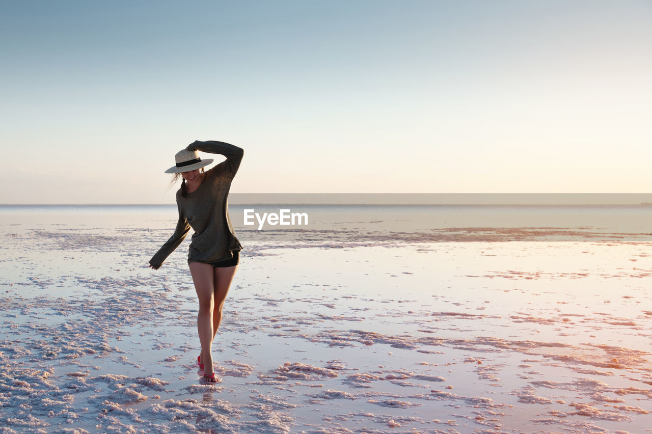 A young caucasian attractive slender woman is walking along a pink sunlit lake balancing on her toes