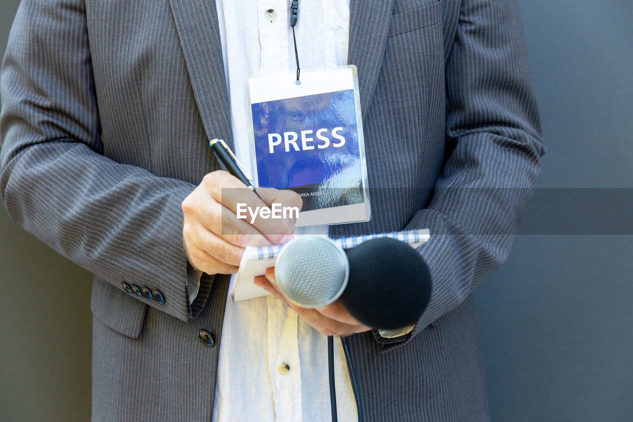 Journalist at media event or news conference, holding microphone, writing notes