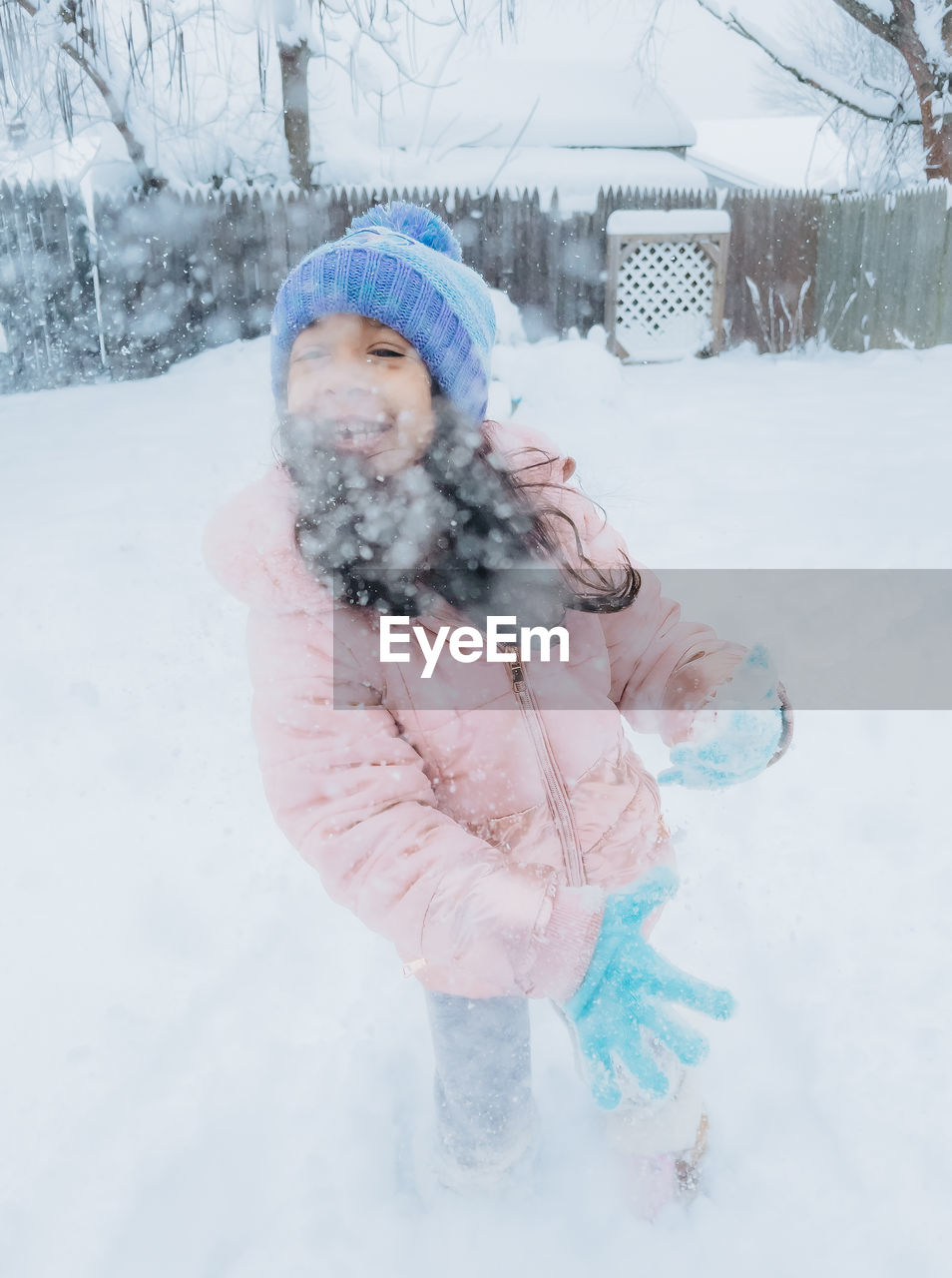 Diverse mixed race pre school toddler girl outdoors in winter playing with snow 