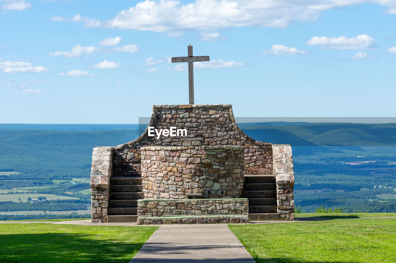 CROSS ON FIELD BY TEMPLE AGAINST SKY