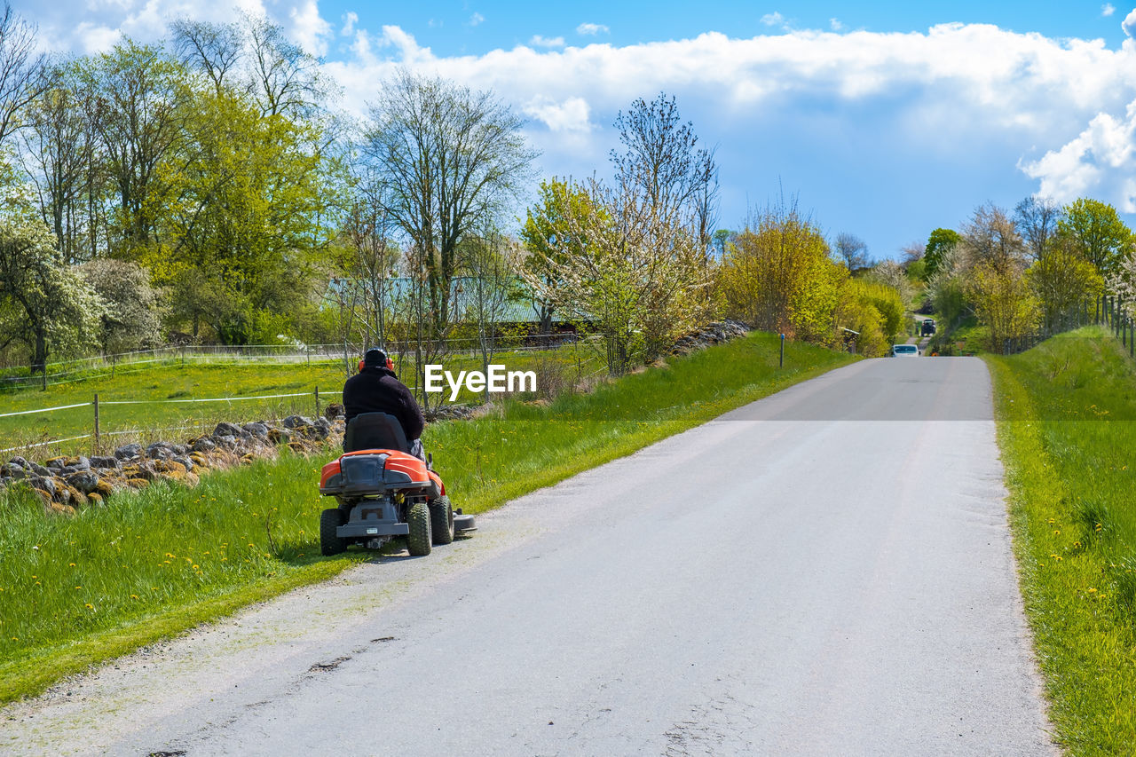 REAR VIEW OF MAN RIDING BICYCLE ON ROAD