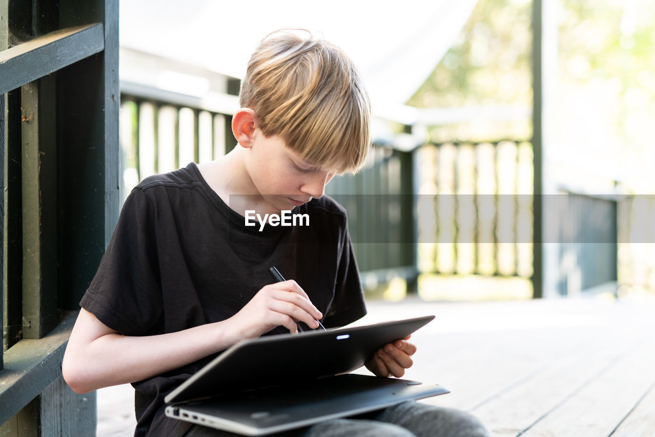 Tween sitting outside on porch using touch screen tablet with stylus