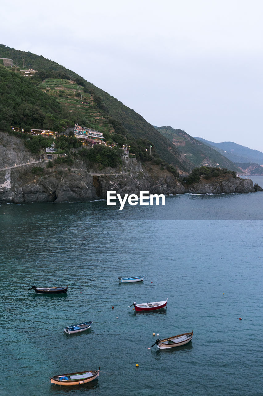 Drone view of fishing boats floating on turquoise water of clean sea near cliffs on cloudy summer day