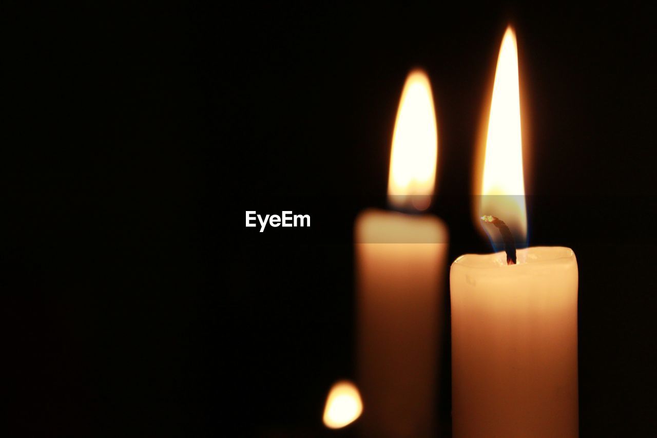 Close-up of burning candles against black background